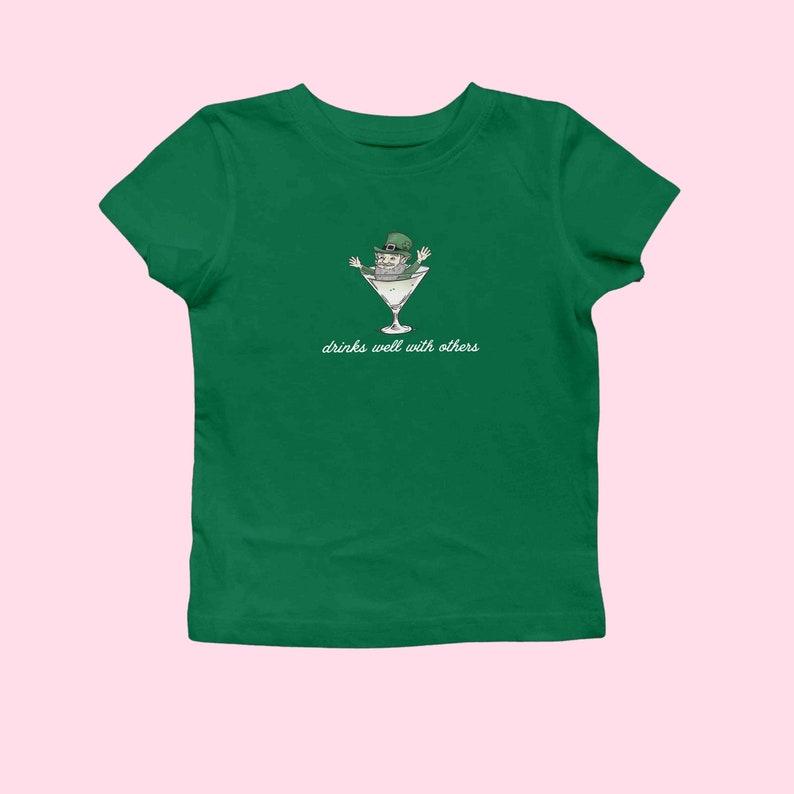 St. Patrick's Day Baby Tee for Women - Leprechaun Martini Cocktail Drinks Well with Others Funny St. Paddy Tee