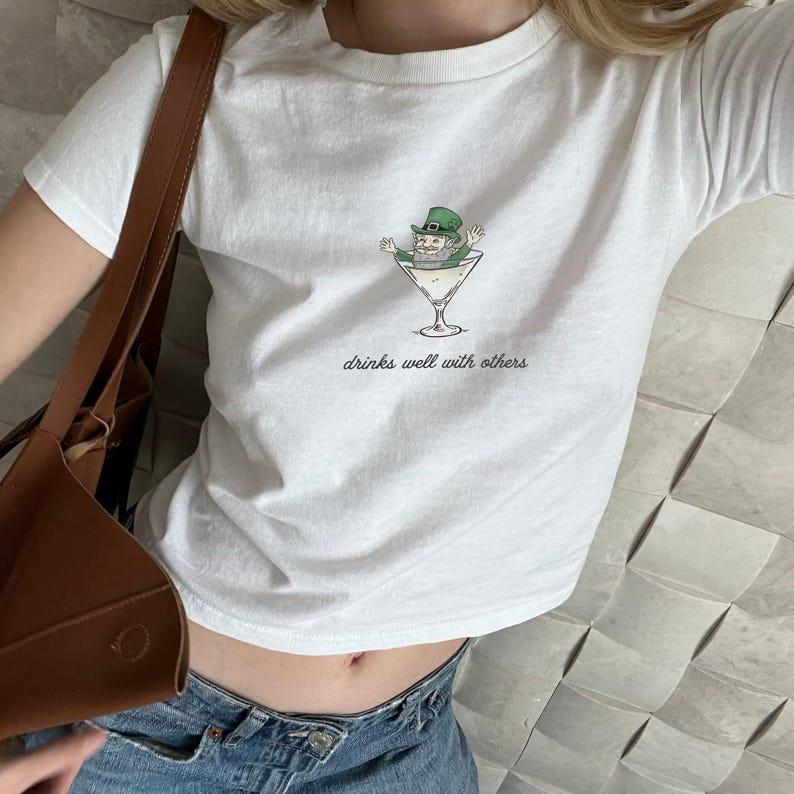 St. Patrick's Day Baby Tee for Women - Leprechaun Martini Cocktail Drinks Well with Others Funny St. Paddy Tee